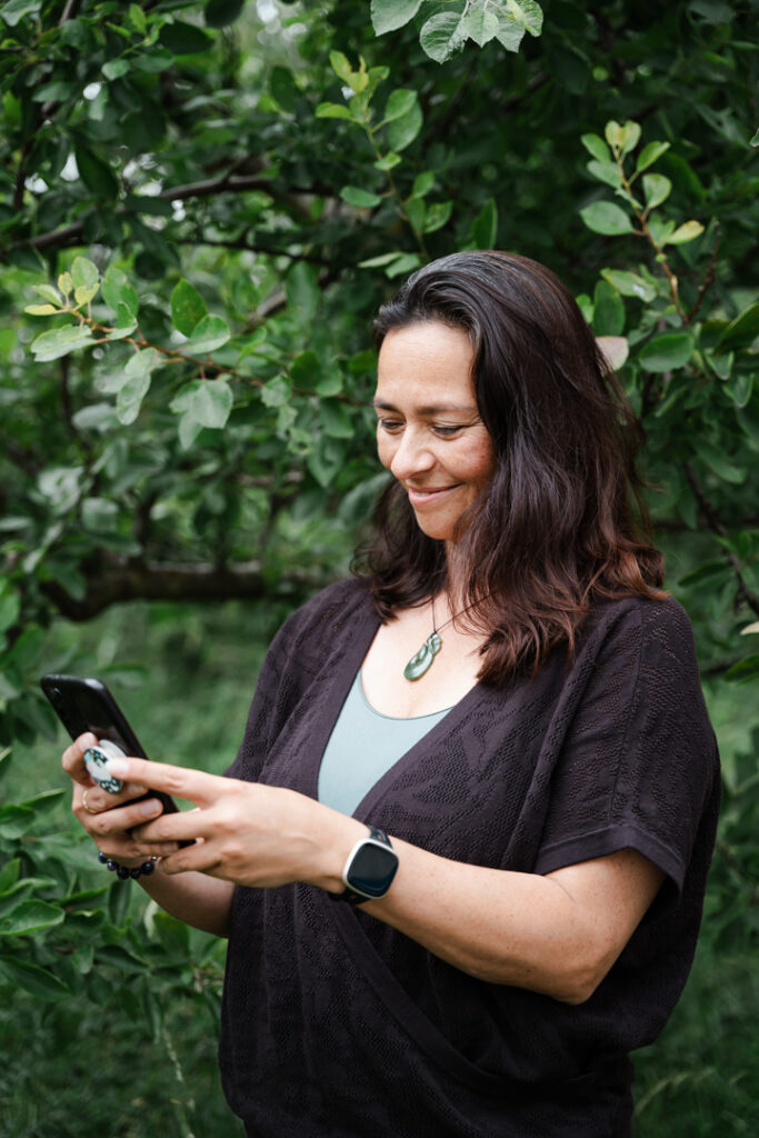 Naomi Bislip bij een boom, glimlachend om iets op haar mobiel