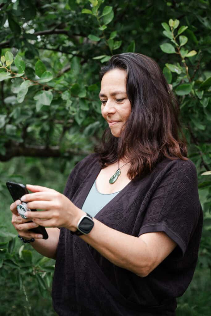 Naomi Bislip, bij een boom, leest iets op haar mobiel